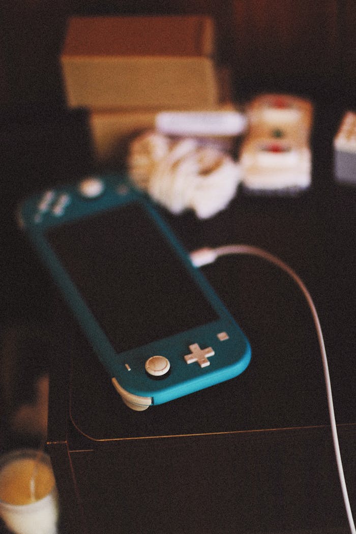 Close-up of a blue Nintendo Switch Lite console charging on a table with gaming accessories in a cozy indoor setting.
